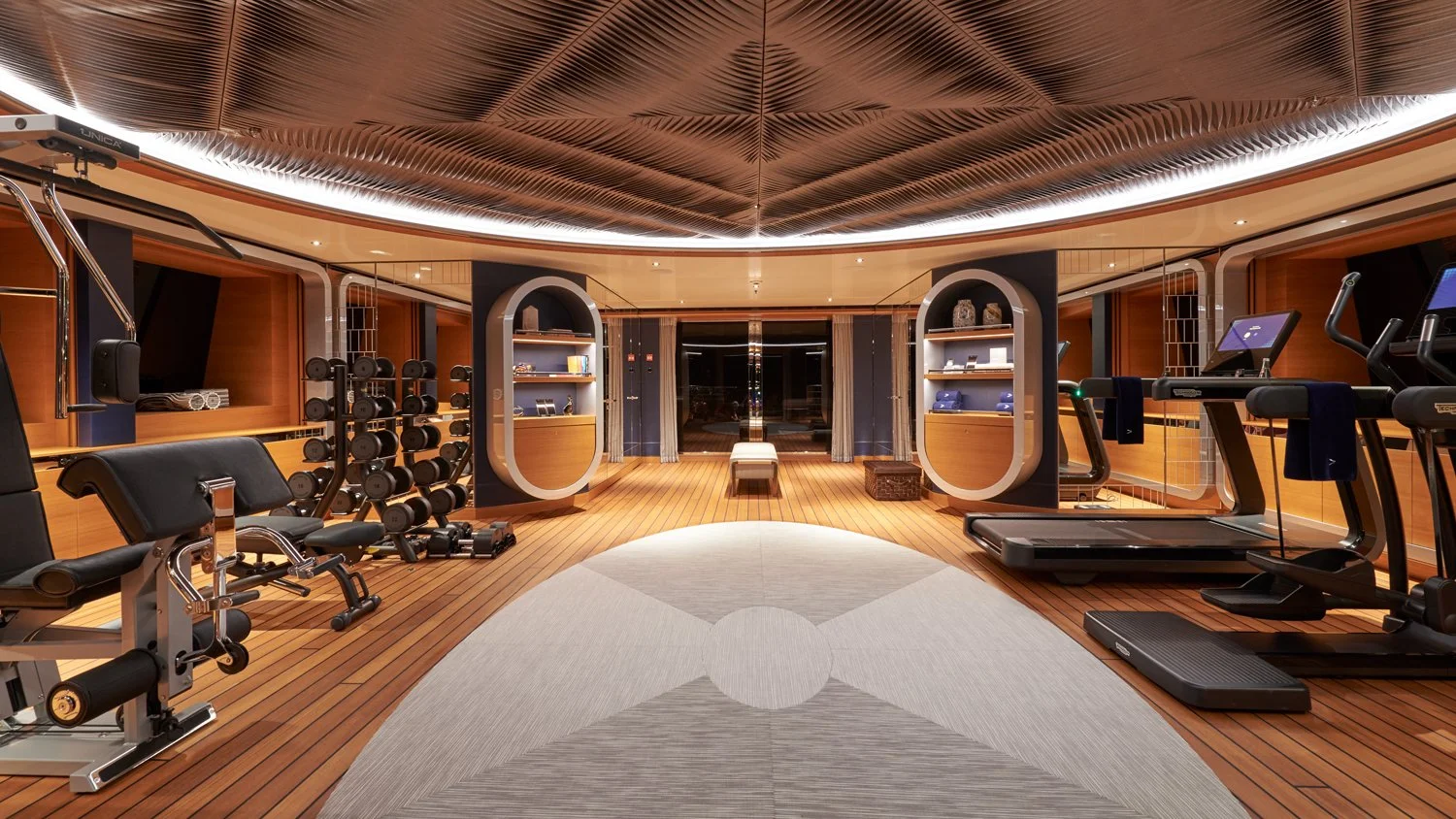 Luxurious home gym with wooden floors, fitness equipment including treadmills, dumbbells, and workout benches, and modern lighting.
