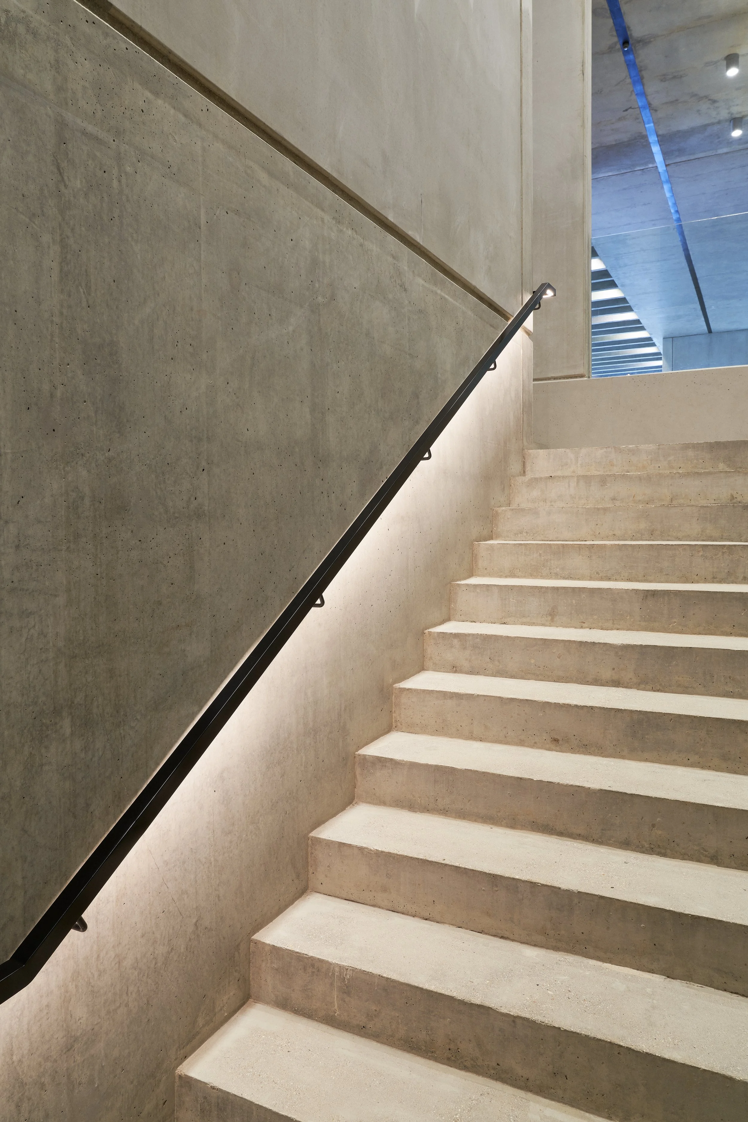 Concrete staircase with black handrail and modern architectural design, illuminated by built-in wall lights.