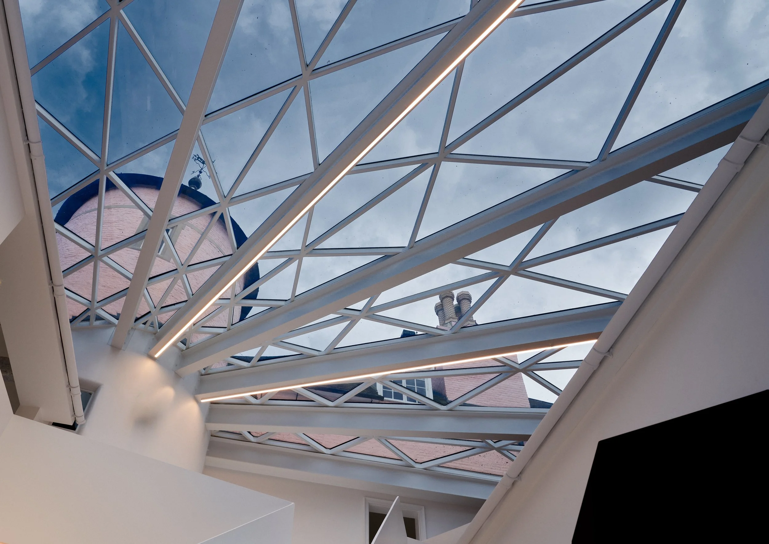 Glass roof with metal framework, partial exterior view of brick building and sky.