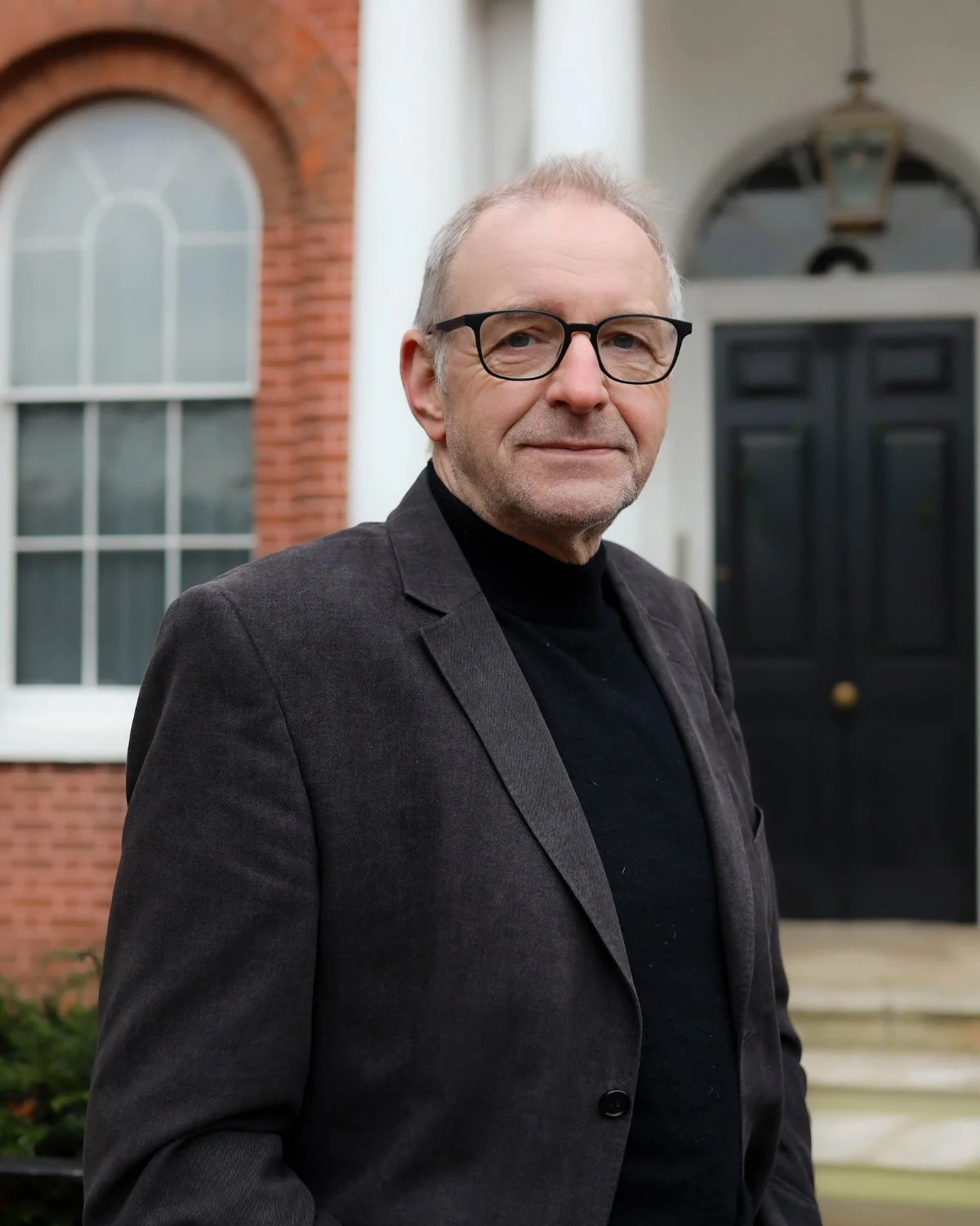 Portrait of a middle-aged man with light hair wearing a striped blue and white shirt, smiling slightly against a blue background.