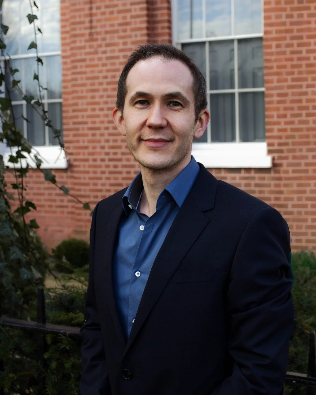 Portrait of a young man with short dark hair, wearing a black t-shirt, smiling slightly against a gradient blue background.