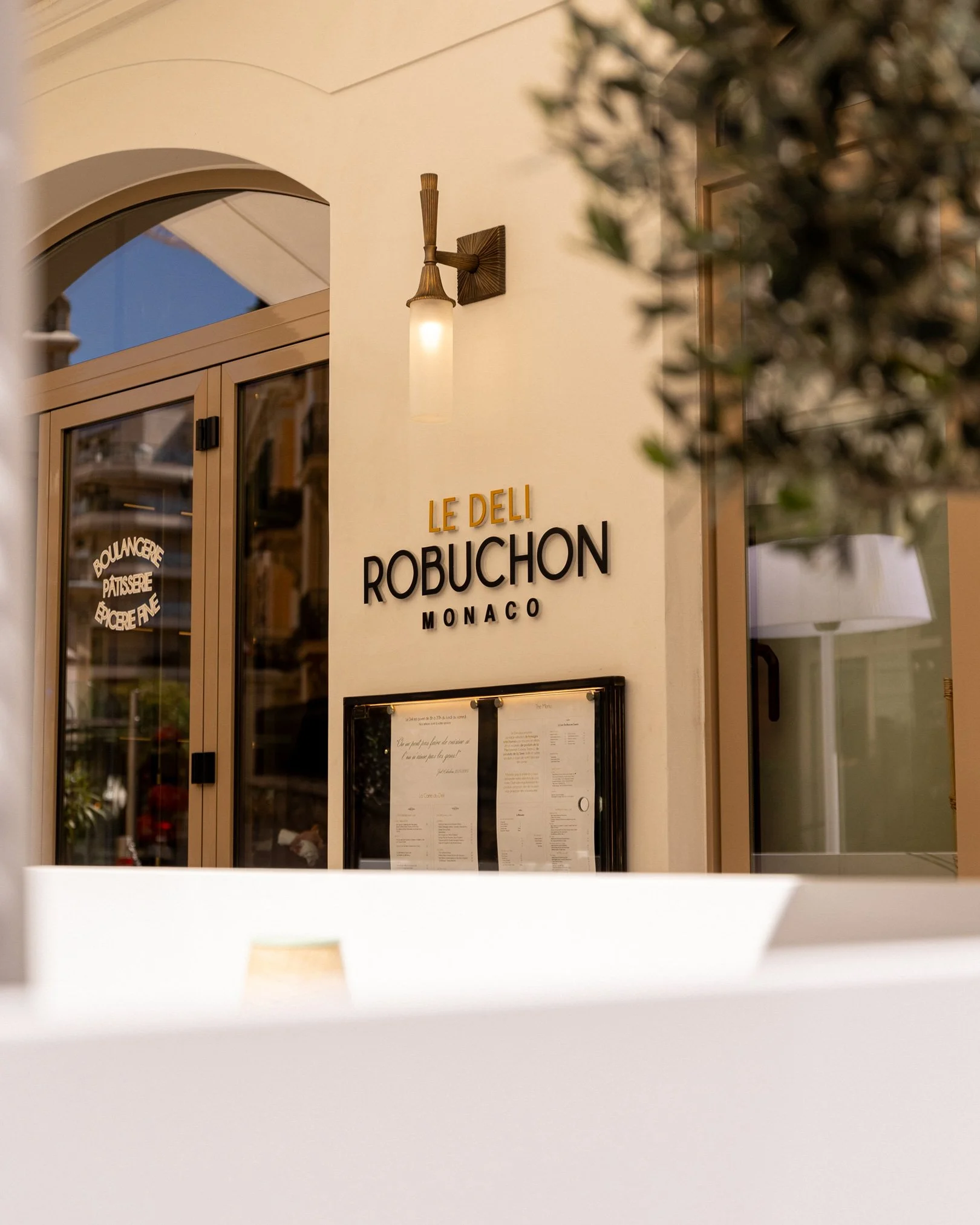 Exterior of Le Deli Robuchon Monaco restaurant with sign and menu display.