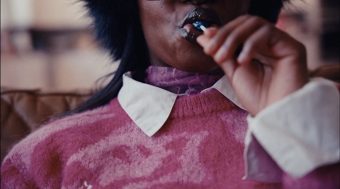 Person wearing a pink sweater and white collared shirt, holding and eating a piece of food.