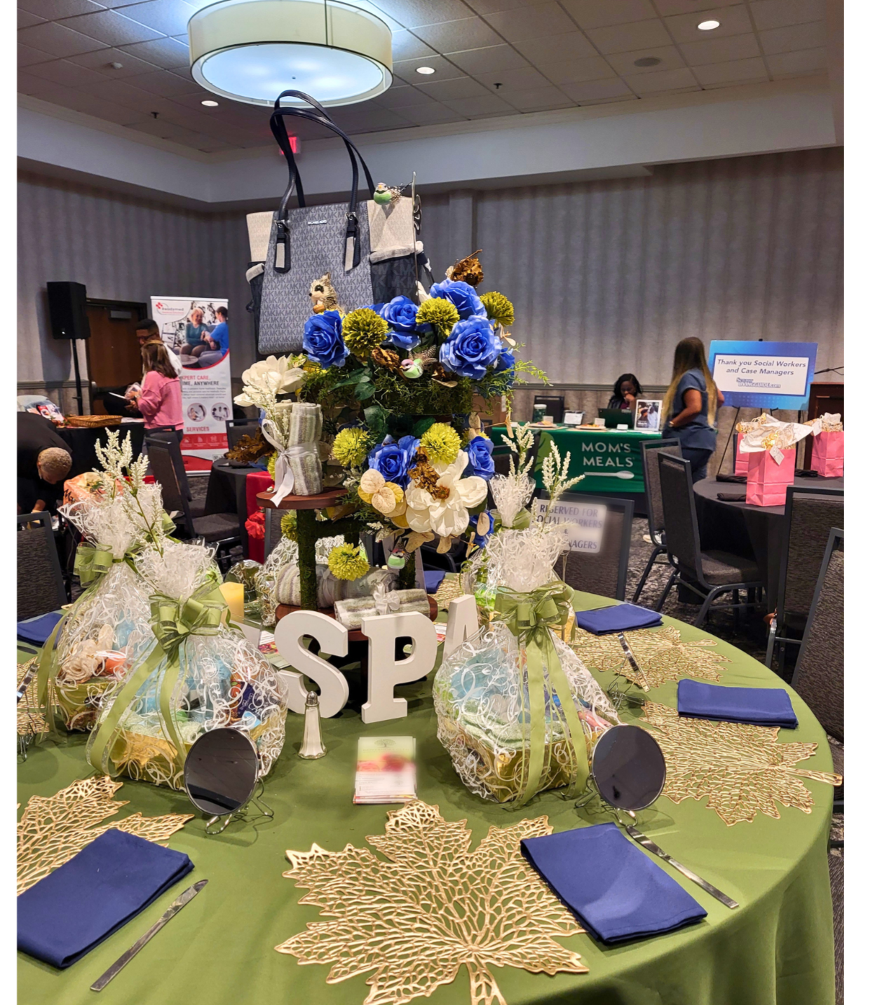 Spa-themed event table with a layered floral centerpiece featuring blue roses, white flowers, greenery, and decorative accents