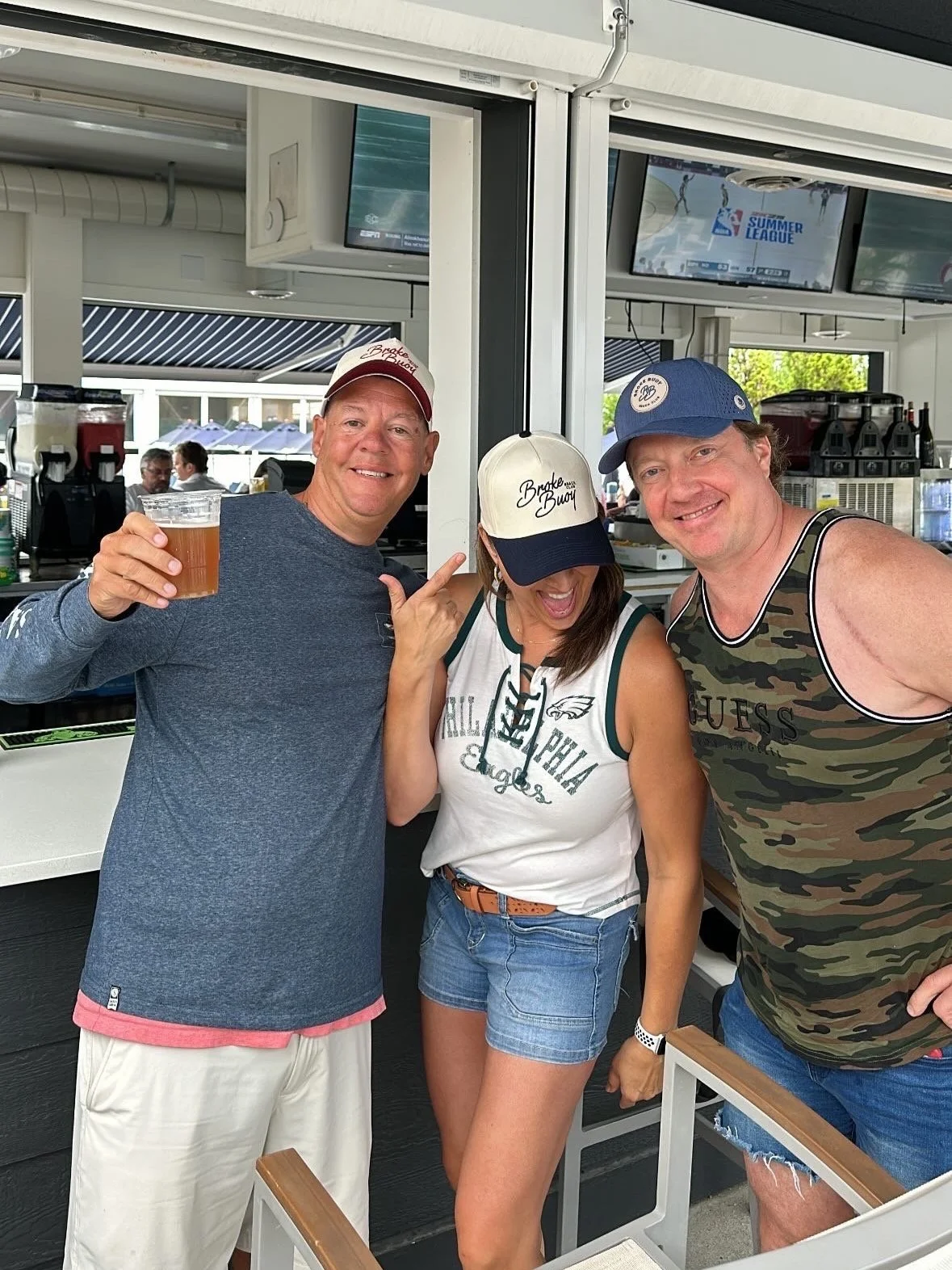 Three friends enjoying drinks together at a bar or outdoor venue, smiling and posing for the photo.