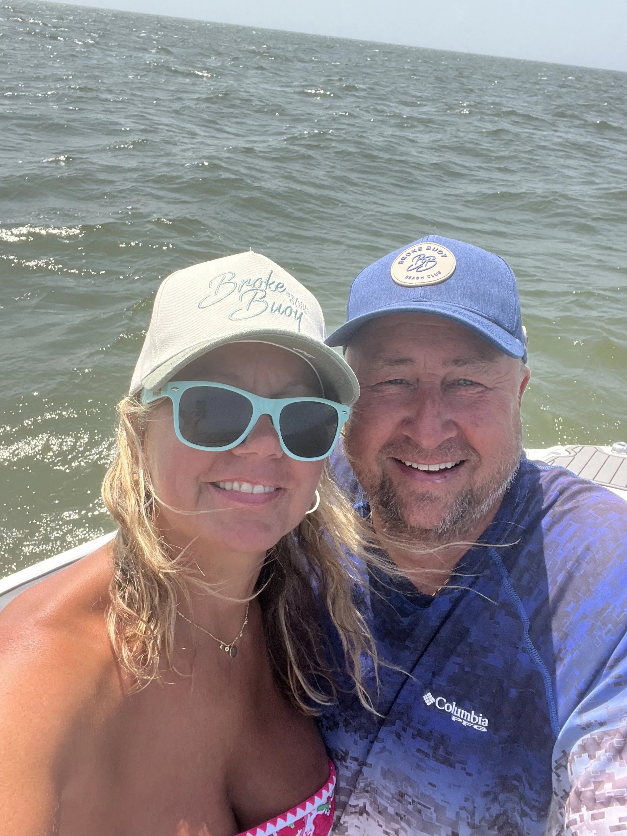 Two people taking a selfie on a boat with water and a slightly cloudy sky in the background.
