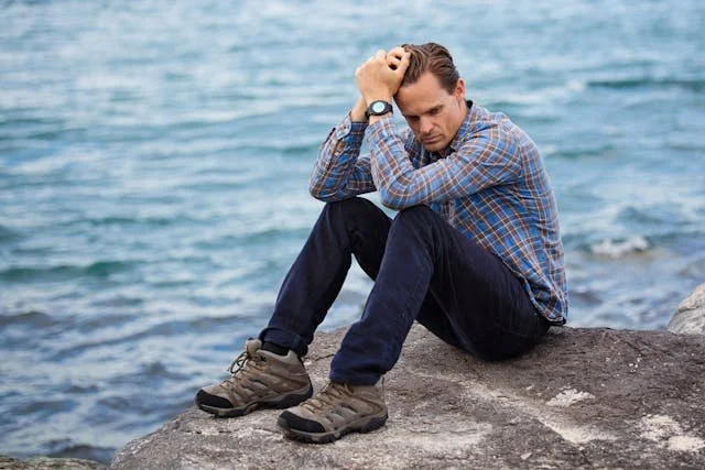 man-wearing-blue-and-maroon-plaid-shirt-sitting-on-a-rock-near-a-body-of-water