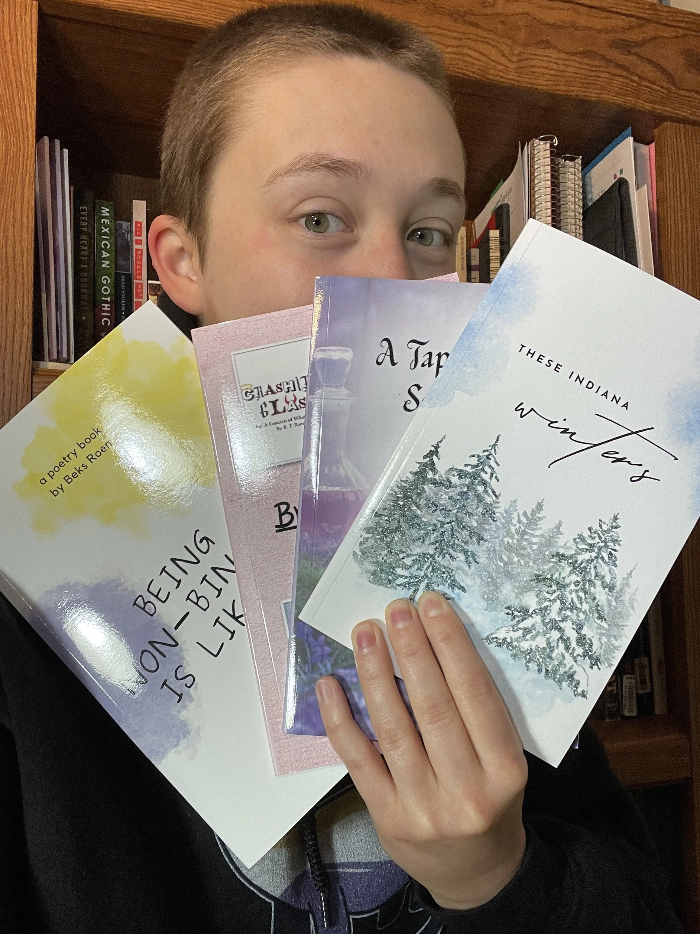 Beks holds print copies of their books "These Indiana Winters," "A Tapestry of Summer Dreams," "Brief Theatricals," and "Being Non-Binary Is Like..."