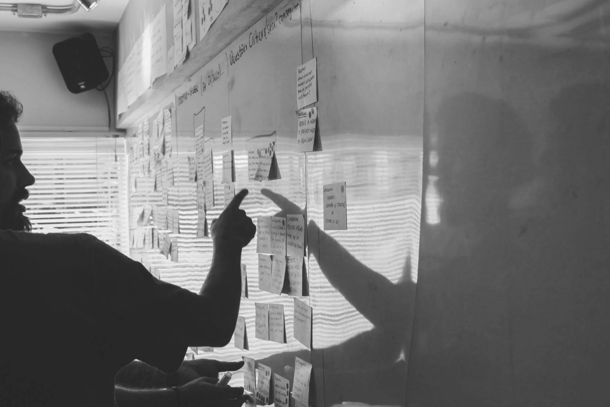 A person pointing at sticky notes posted on a wall during a discussion or planning session.