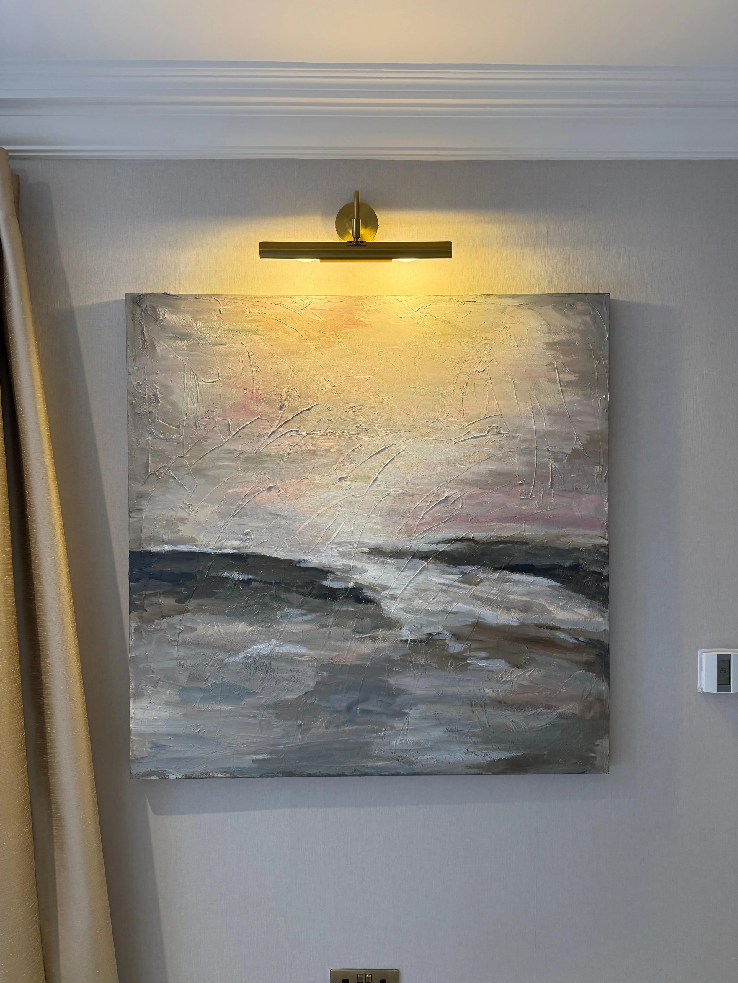 Abstract painting of a seascape with textured brushstrokes depicting waves at sunset, mounted on a wall with a light fixture above it.