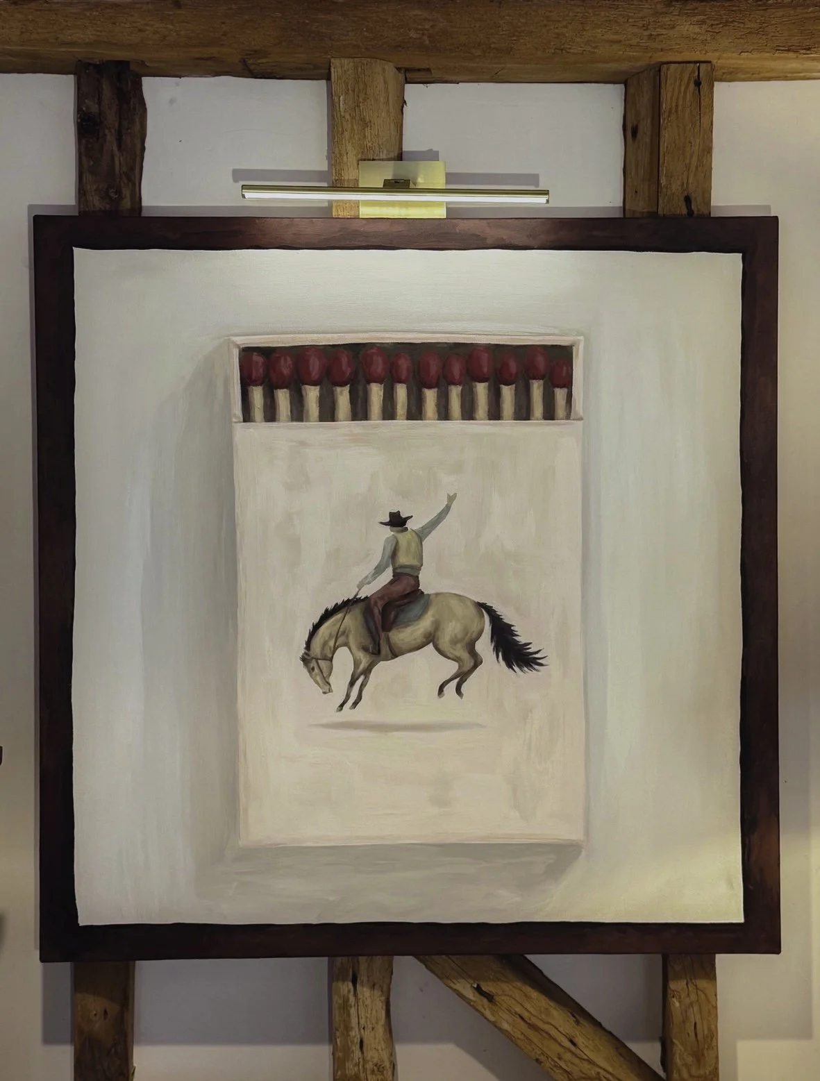 Painting of a cowboy riding a horse and reaching to grab red apples that are hanging from a horizontal line of sticks.