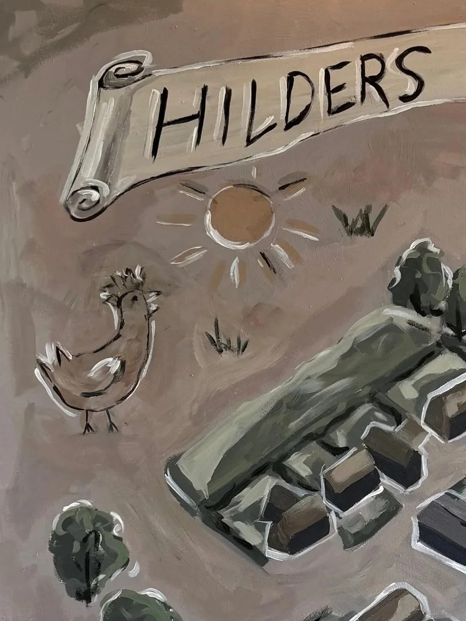 A painted sign with the word 'HILDERS' on a scroll banner. A cartoon-style chicken, a sun, some small bushes, and part of a keyboard are also depicted in the painting.