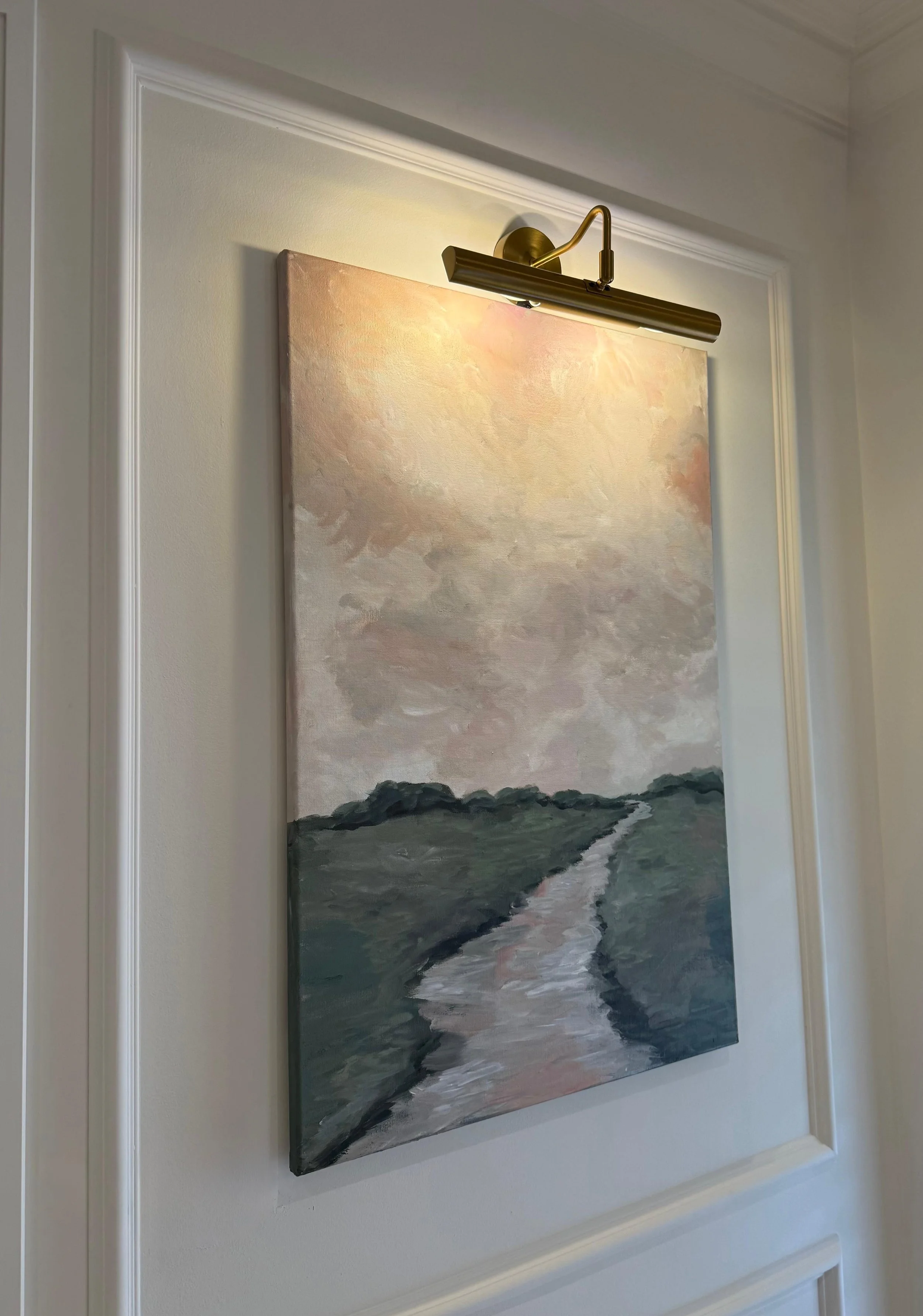 A landscape painting of a river flowing through rocky terrain during sunset, illuminated by a wall-mounted light fixture.