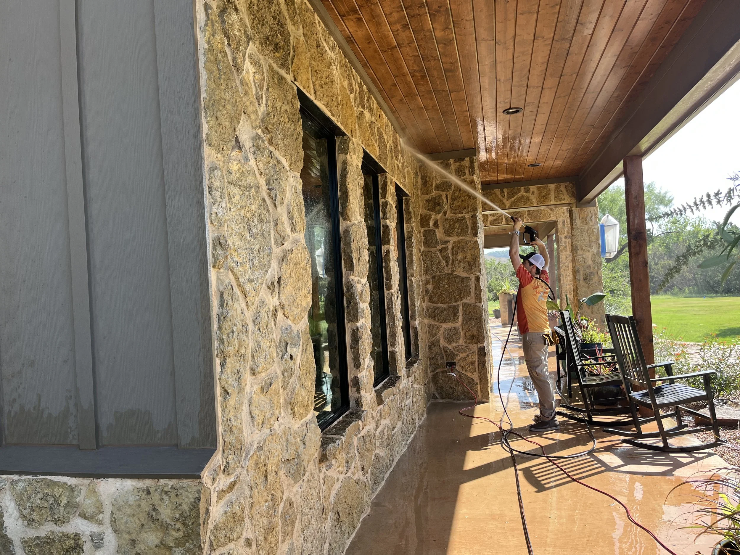 Man soft washing a concrete porch in front of a brick house.