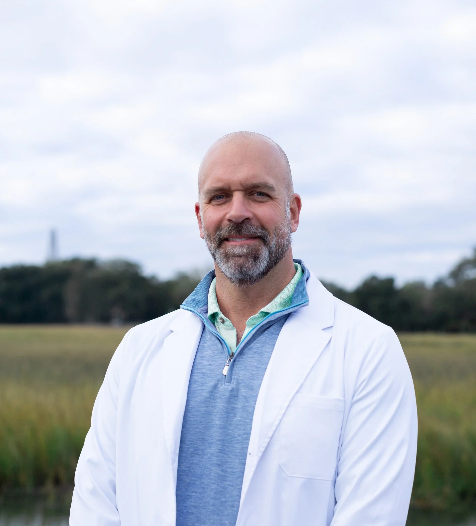 Headshot of Chad against a marshy background and cloudy sky.