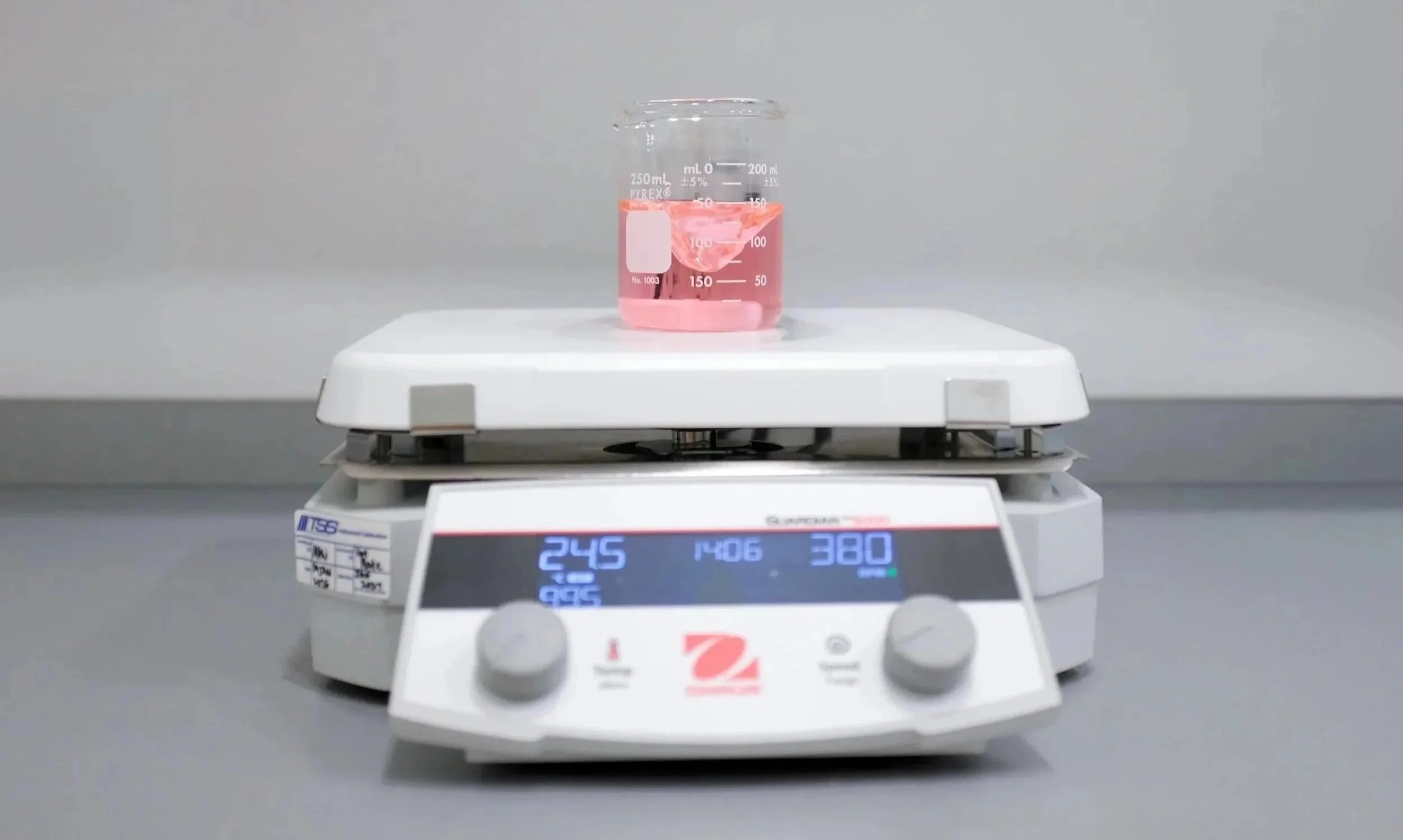 A laboratory hotplate/stirrer with a beaker containing pink liquid on top, used for heating and stirring chemical solutions.