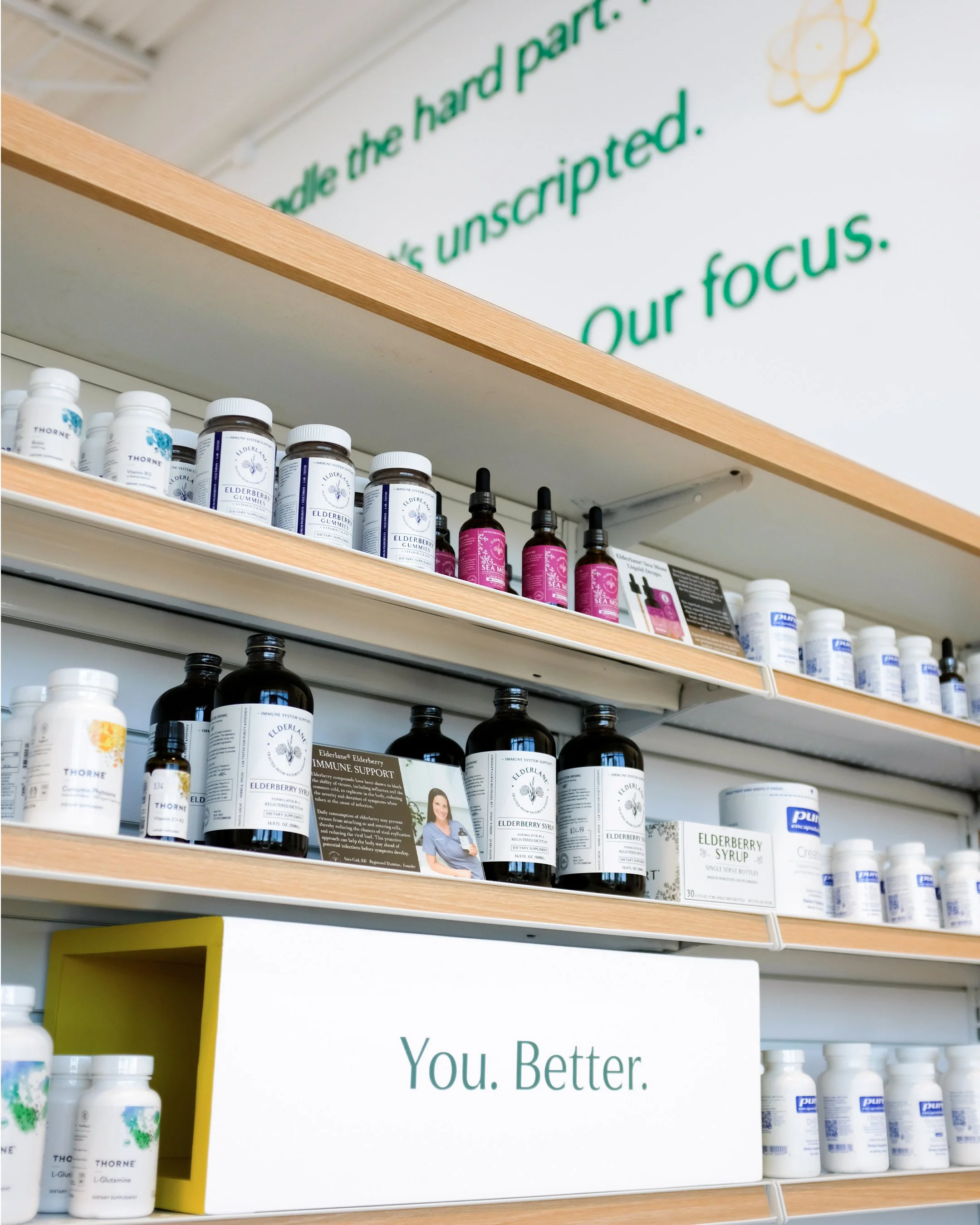 Shelves stocked with bottles of Elderberry supplement, syrup, and other health products in a store or pharmacy. There is a sign that reads 'You. Better.' in front of the shelves.