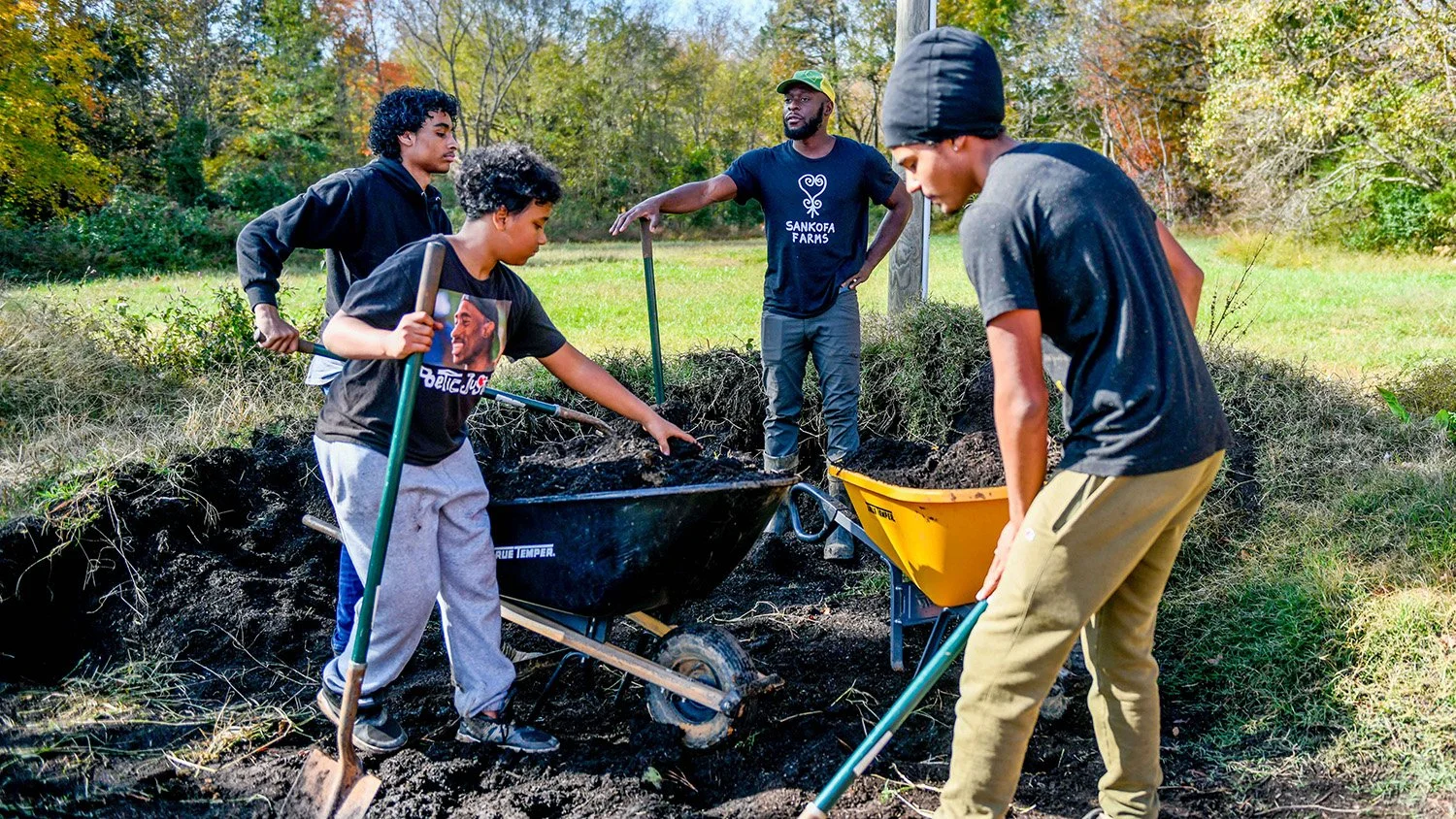 Group of five people planting trees outdoors with shovels and wheelbarrows during daytime