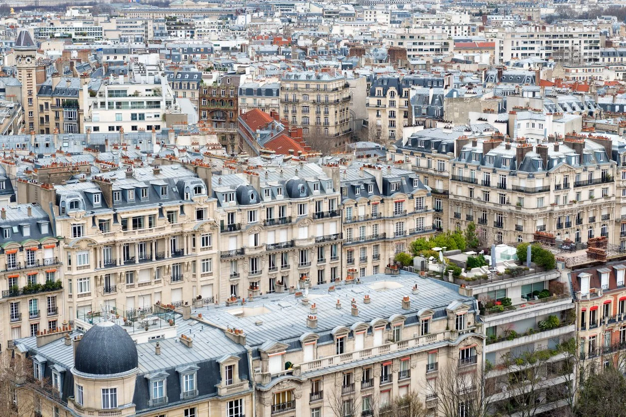 Aerial view of densely packed Parisian apartment buildings with classic French architecture, mansard roofs, and rooftop terraces in a cityscape.