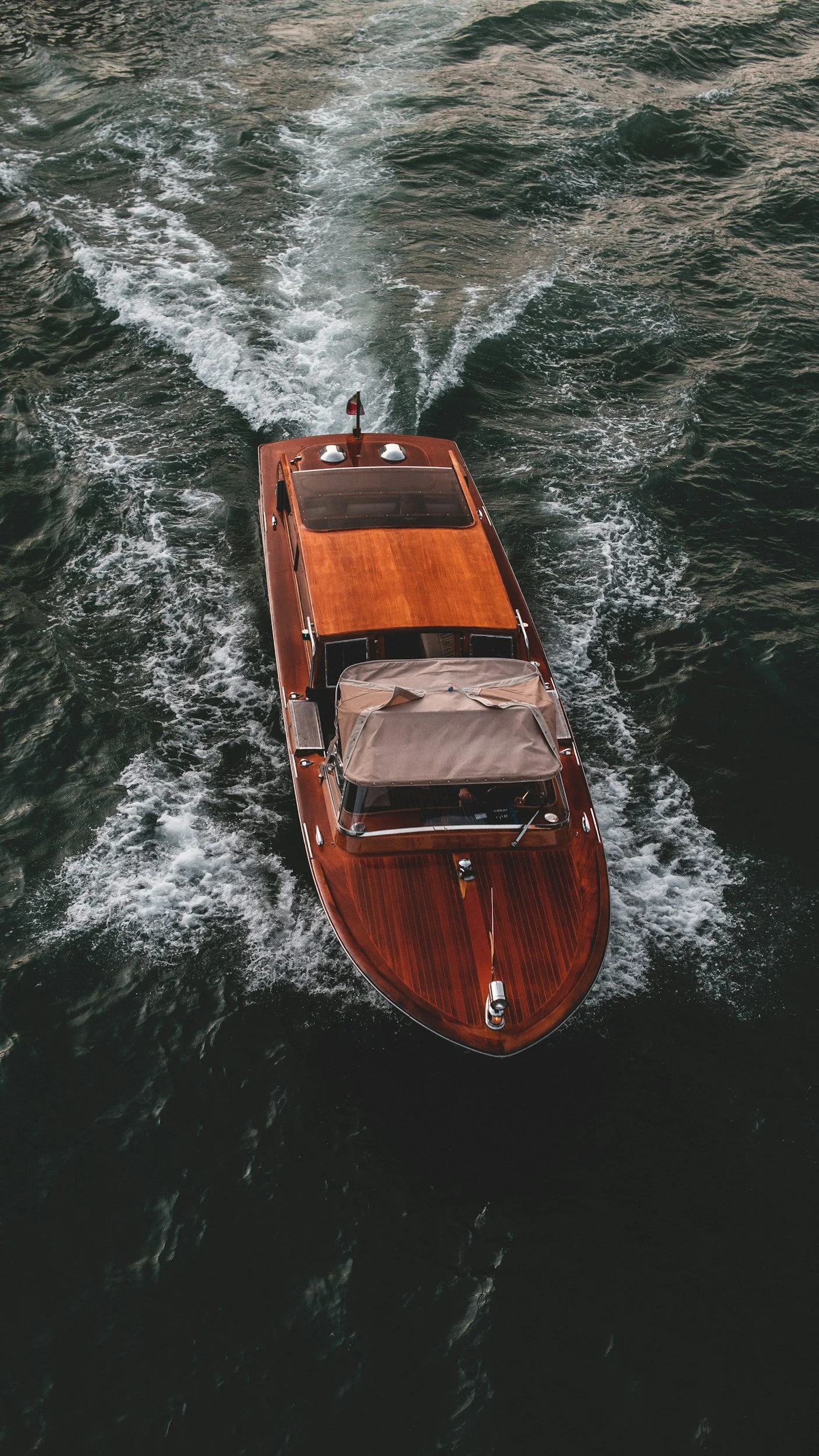 A wooden motorboat cutting through water, creating a wake behind it.