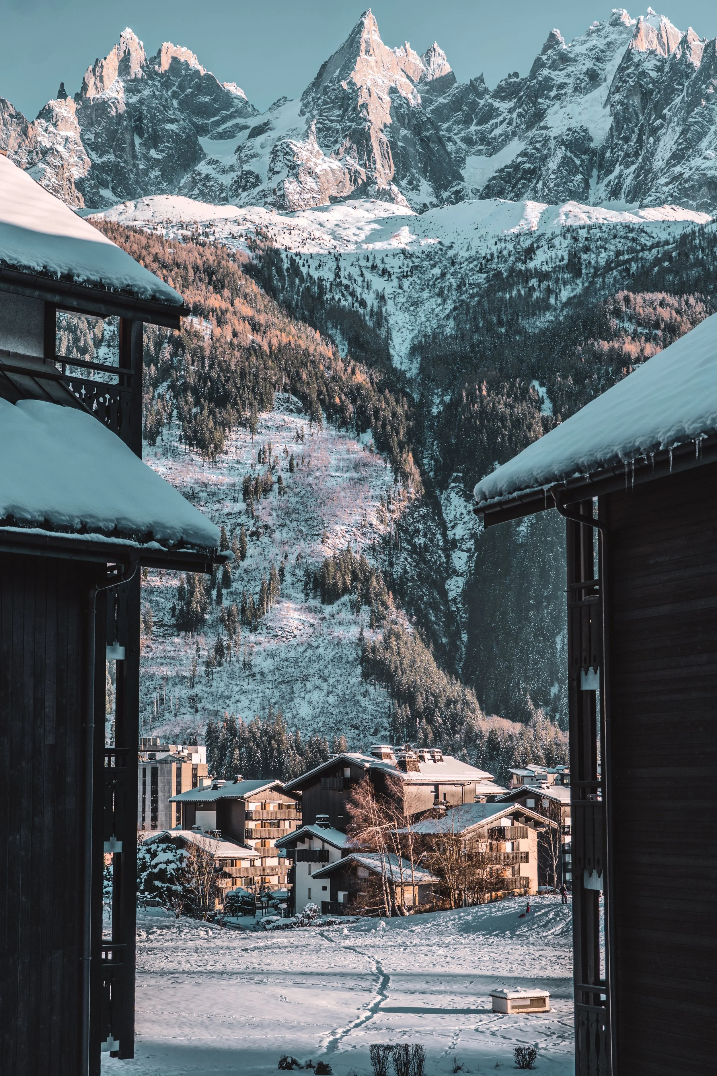 View of snow-covered mountains and a small town with residential buildings, seen from a balcony in a snowy setting.