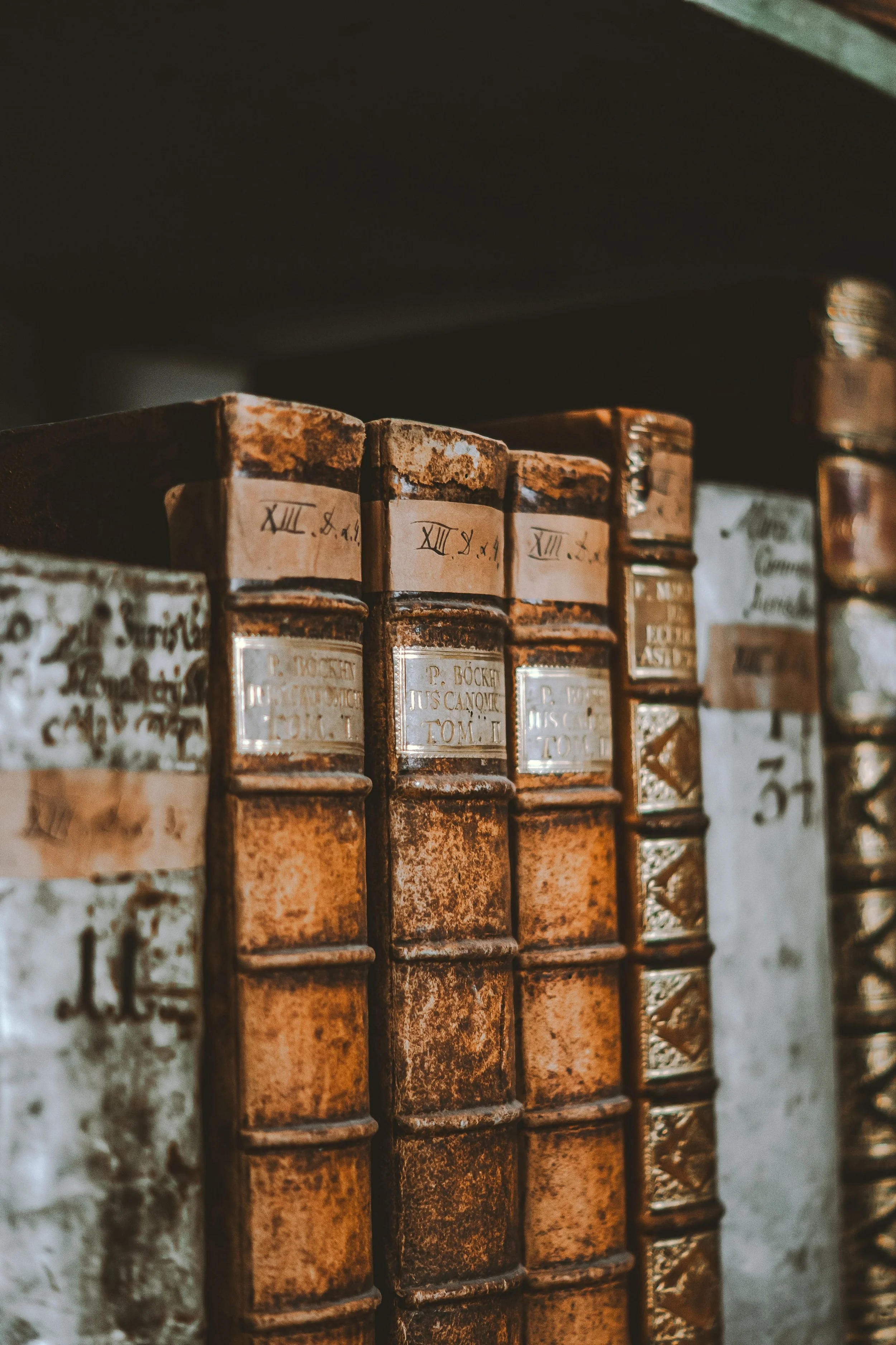 Close-up of old, worn antique books with handwritten labels on their spines, on a shelf.