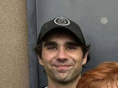 Close-up of a smiling man wearing a black baseball cap.