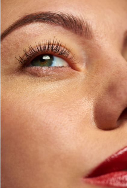 Close-up of a person receiving eyelash extension application, with tools used for attaching synthetic eyelashes to natural lashes.