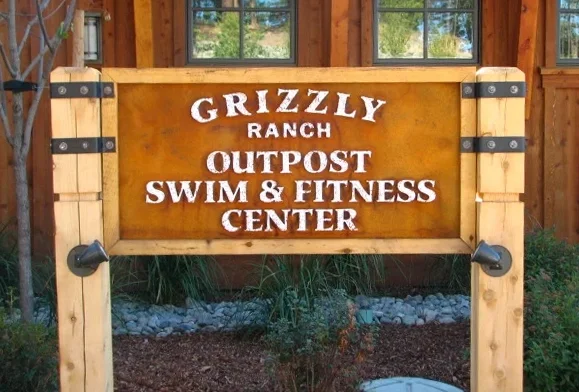 Wooden sign for Grizzly Ranch Outpost Swim & Fitness Center in a rustic setting.