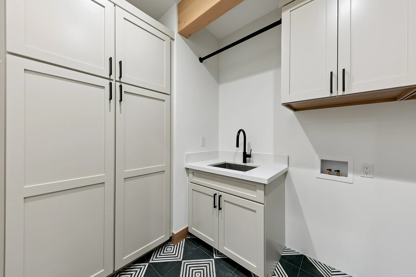 Modern laundry room with abundant white cabinetry, a compact sink, black fixtures, and a black and white tiled floor.