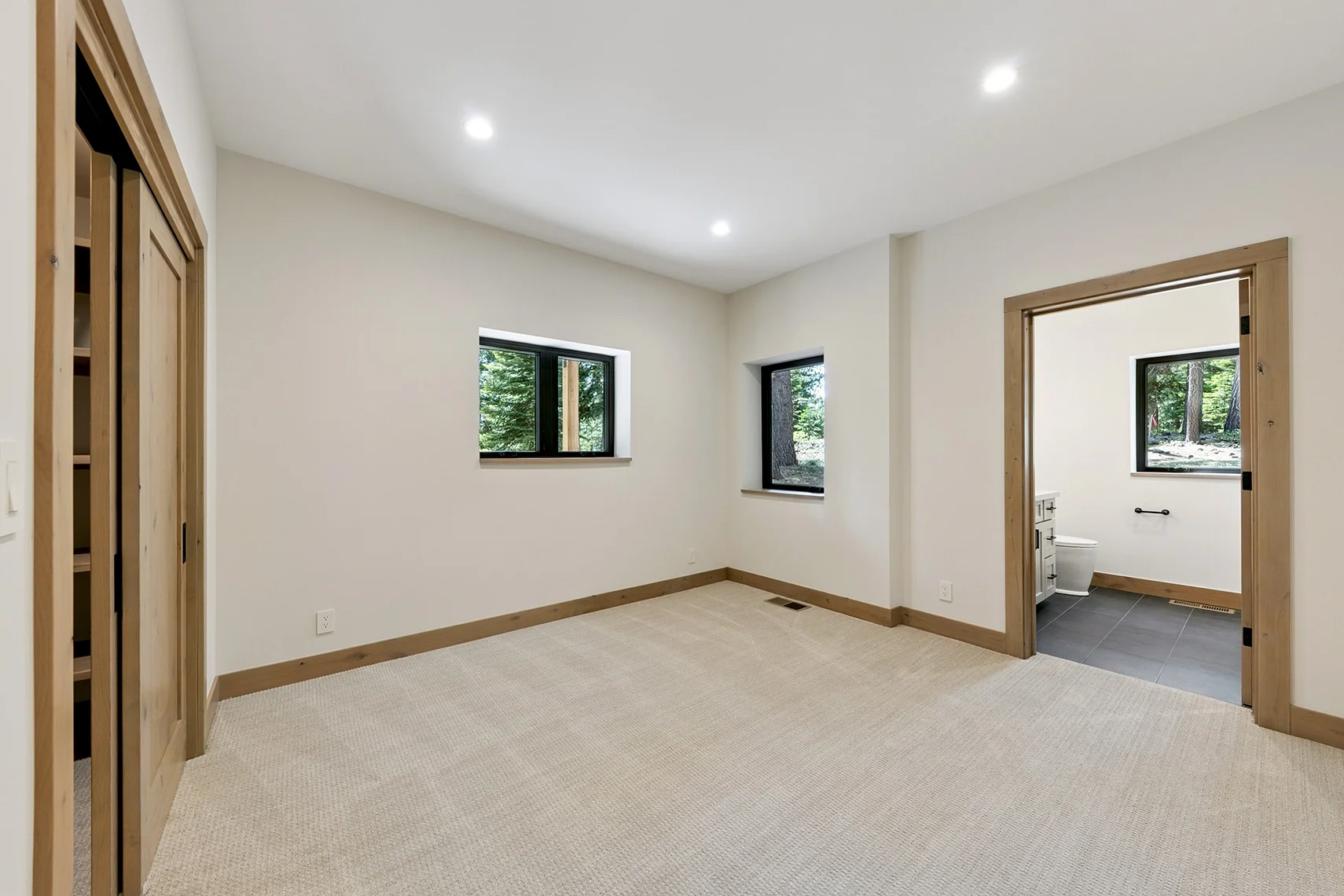 Modern bedroom with white walls, light carpeting, two small windows, and a built-in closet with an attached bathroom.