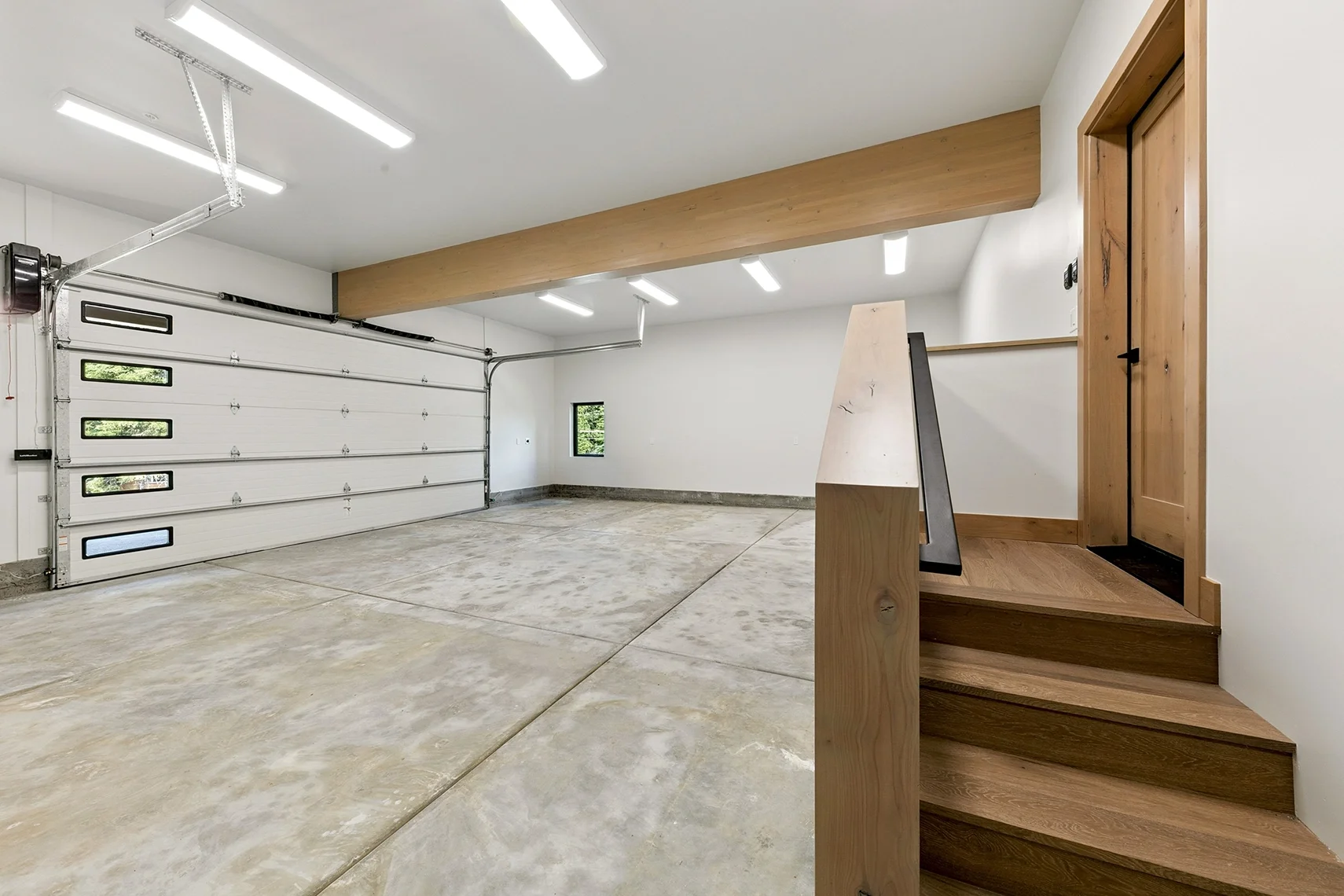 Modern two-car garage with a two-bay door featuring small horizontal windows, a concrete slab, wood stairs, and a walkway leading to the home entrance.