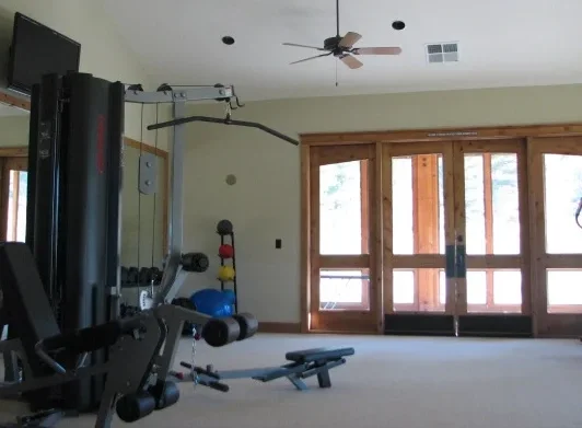 Empty room with home gym equipment, ceiling fan, large glass doors, light green walls, and beige carpet.