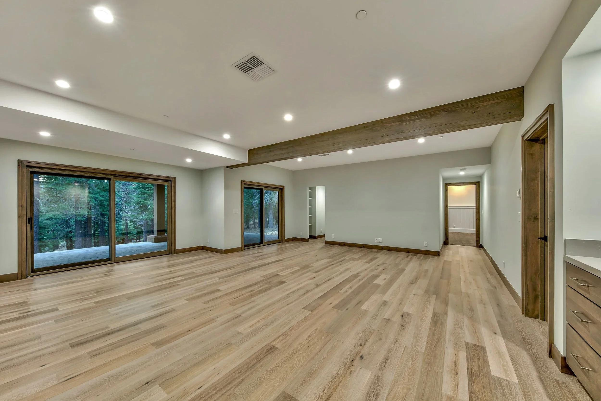 Spacious empty living room with hardwood floors, large sliding glass doors, and white walls.