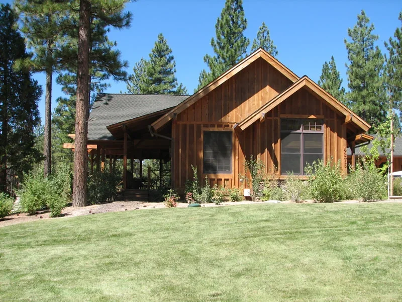 A wooden house with a large front yard, surrounded by trees, with a clear blue sky overhead.