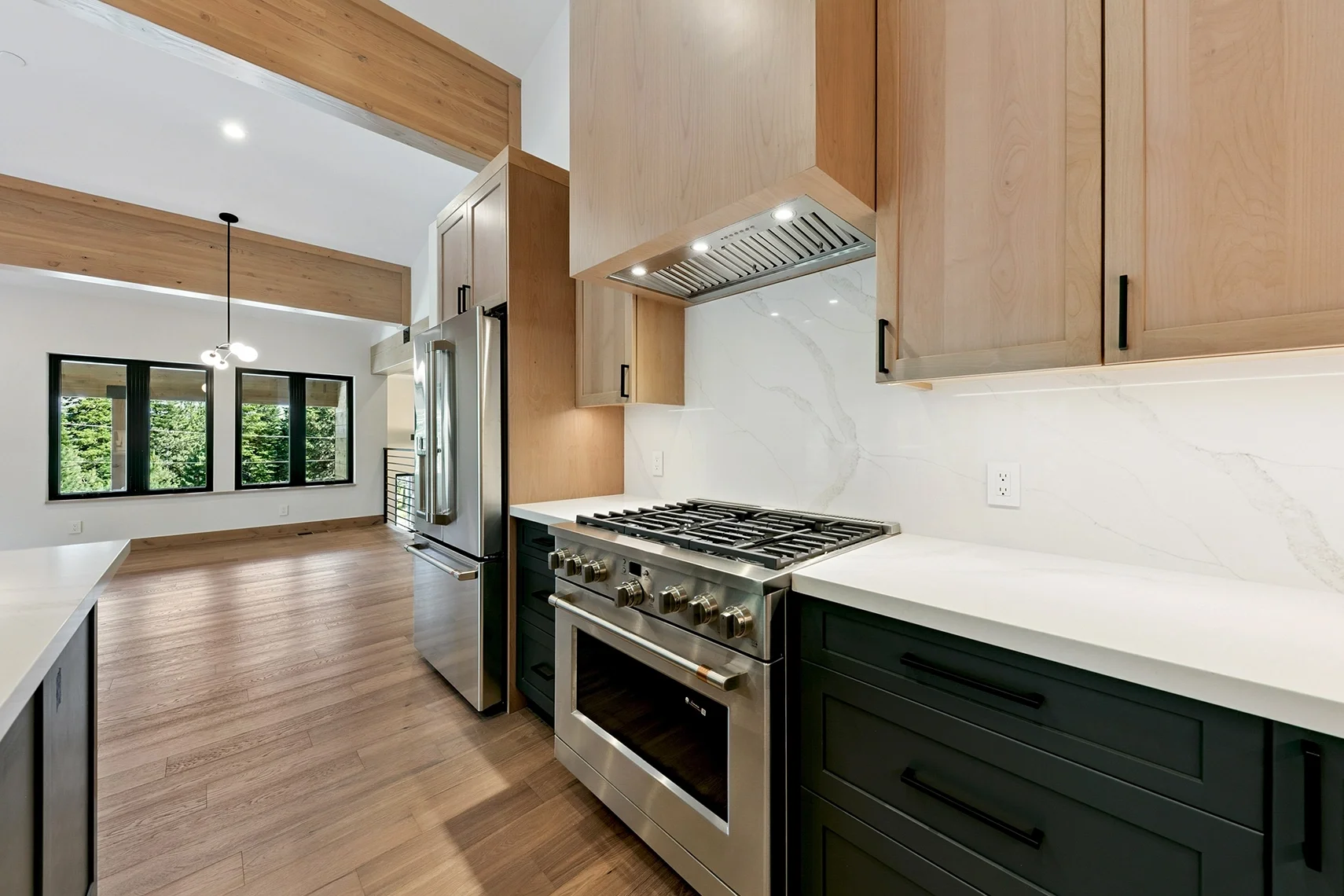 Modern kitchen with natural wood flooring, stainless steel appliances, black lower cabinets, natural wood upper cabinets, and a white marble backsplash.