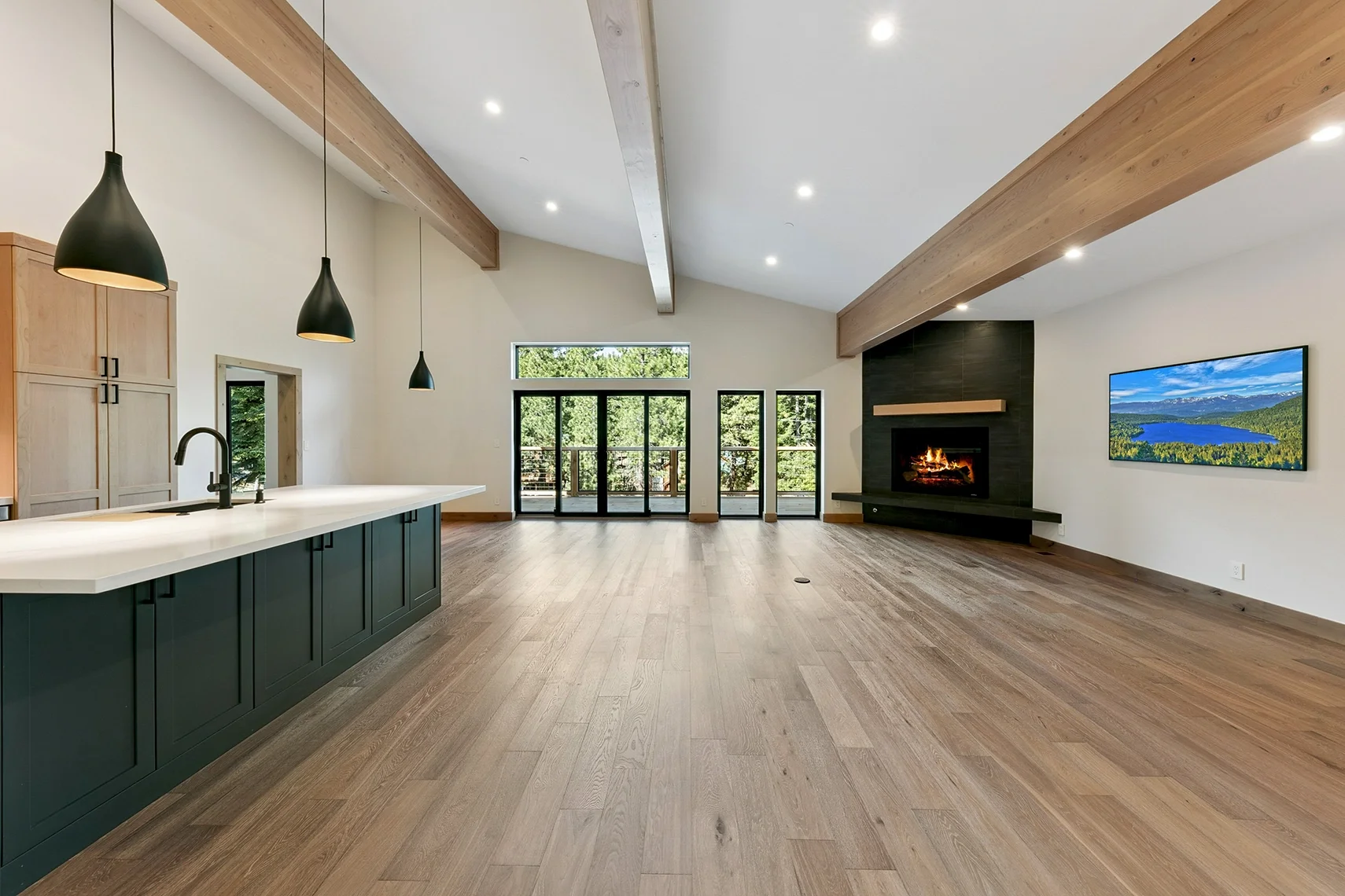 Modern mountain kitchen featuring dark blue cabinetry, a large white countertop island, black pendant lighting, and an open-concept living space with sliding glass doors.