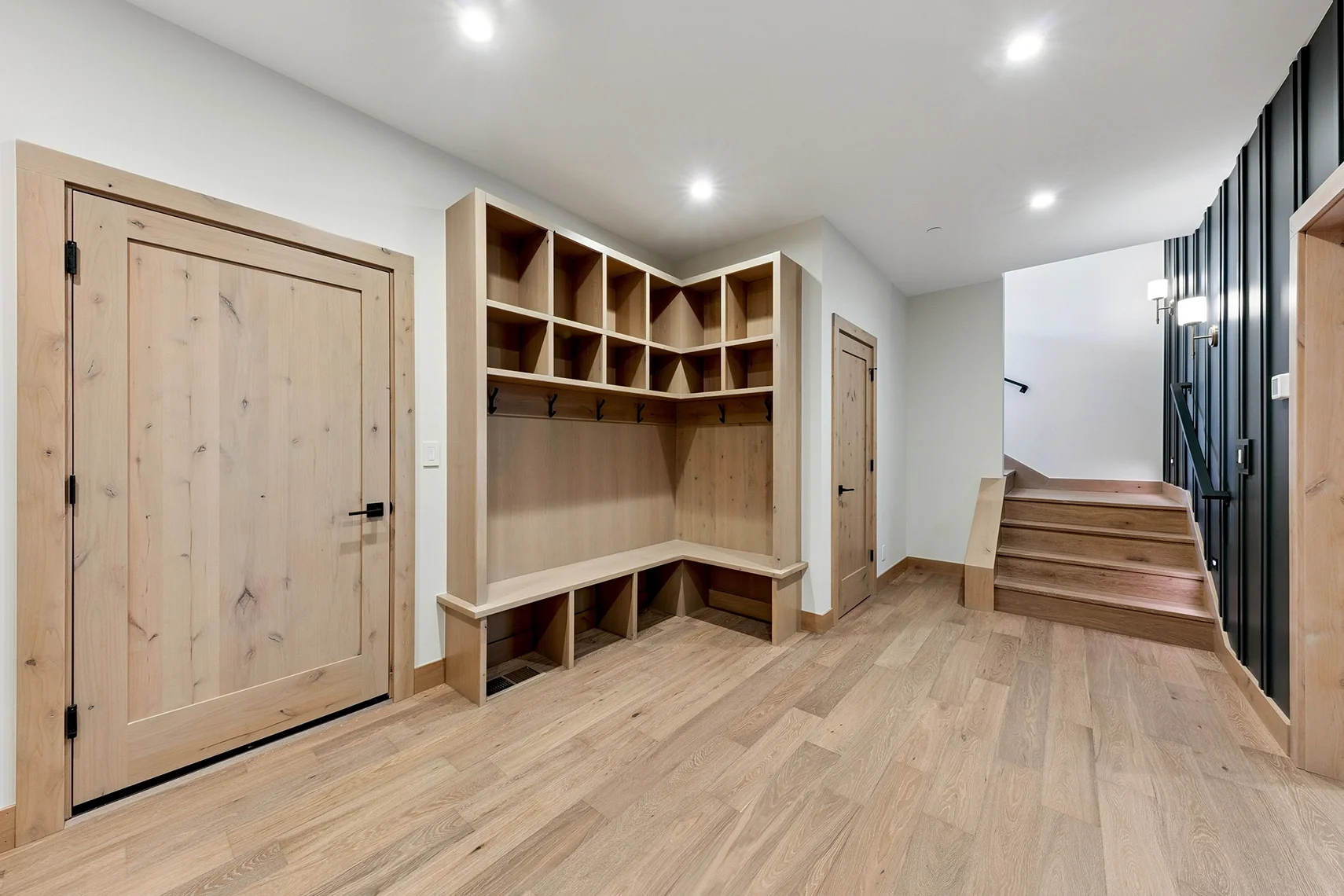 Spacious modern mudroom with light natural wood flooring, built-in storage, and stairs leading to the upper level.