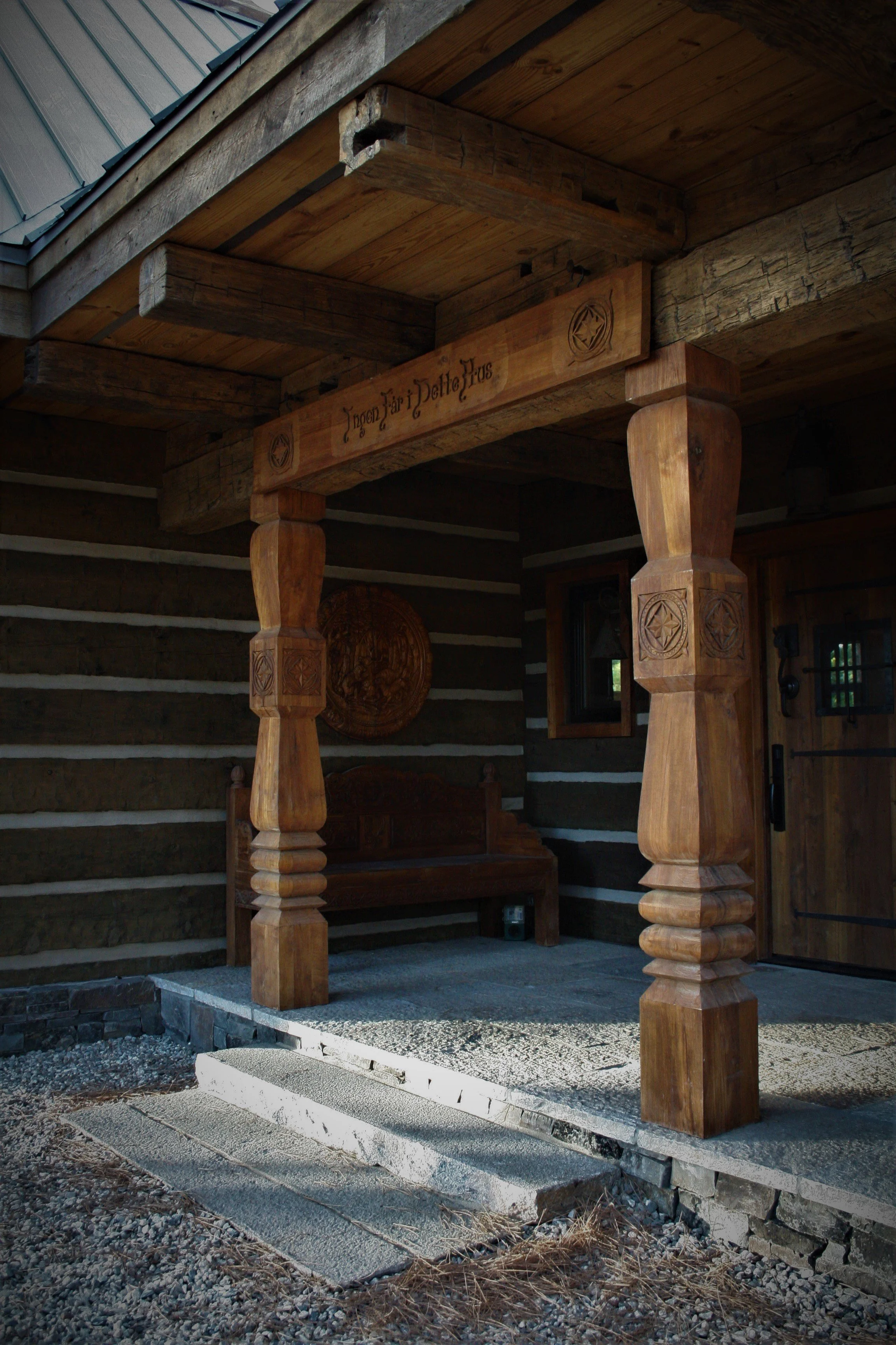 Wooden porch with carved columns and a bench against log cabin wall.
