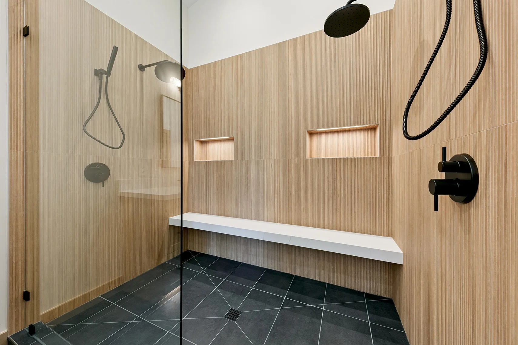 Modern walk-in shower with black tile flooring, bamboo-look wood tile walls, black fixtures, and a glass partition.
