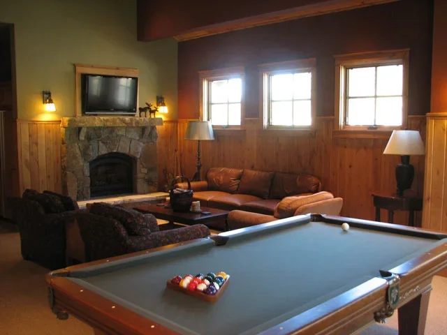 Living room with a pool table, a stone fireplace, a wall-mounted TV, and multiple windows with wooden blinds.