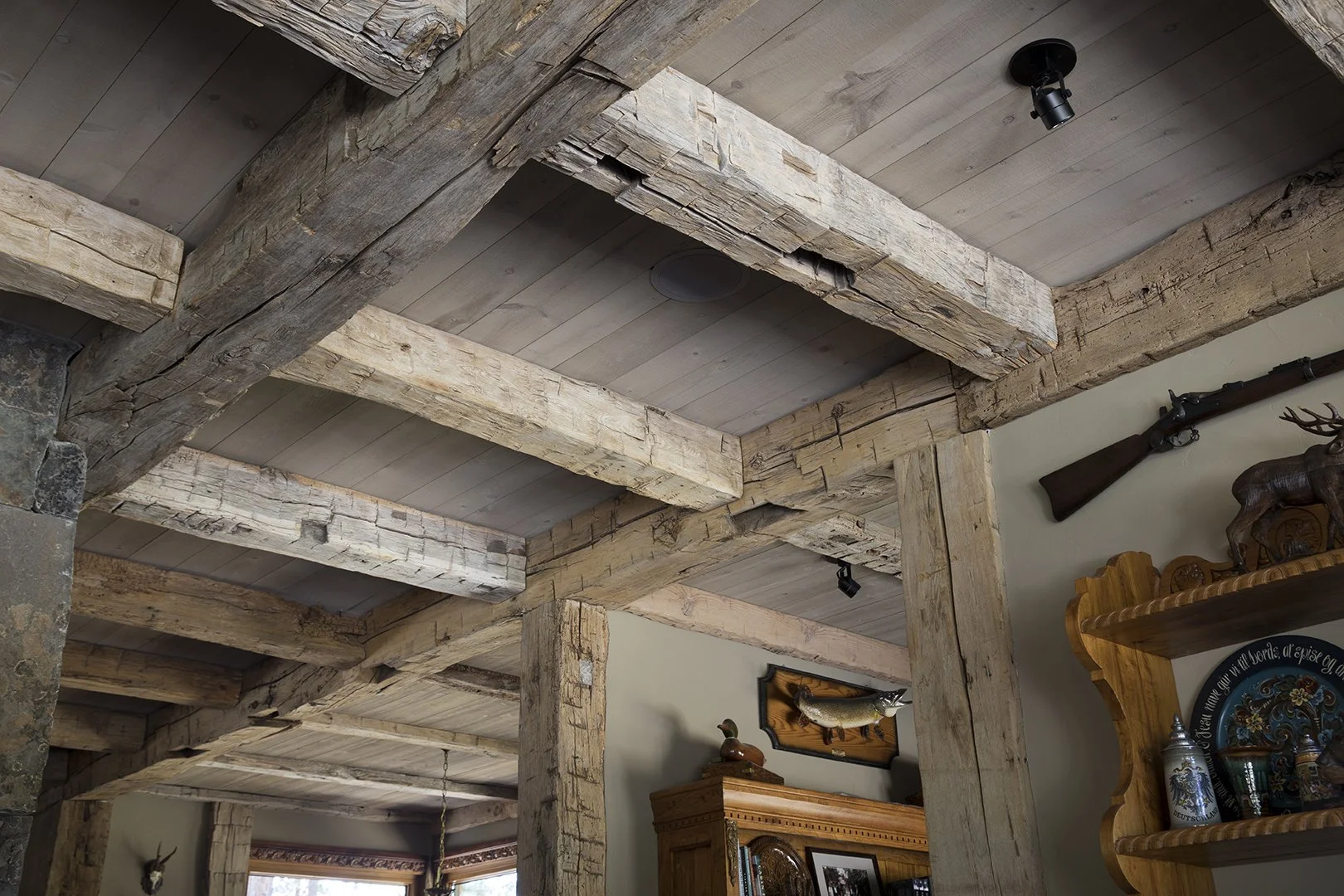 Interior shot of a rustic room with exposed wooden beams and a wooden ceiling, part of a living space with decorative items and a mounted fish on the wall.