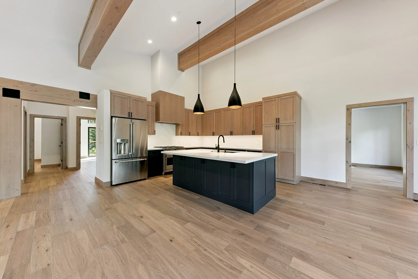 Modern open-concept kitchen with black pendant lights, a large island with a white countertop, and exposed wood ceiling beams.