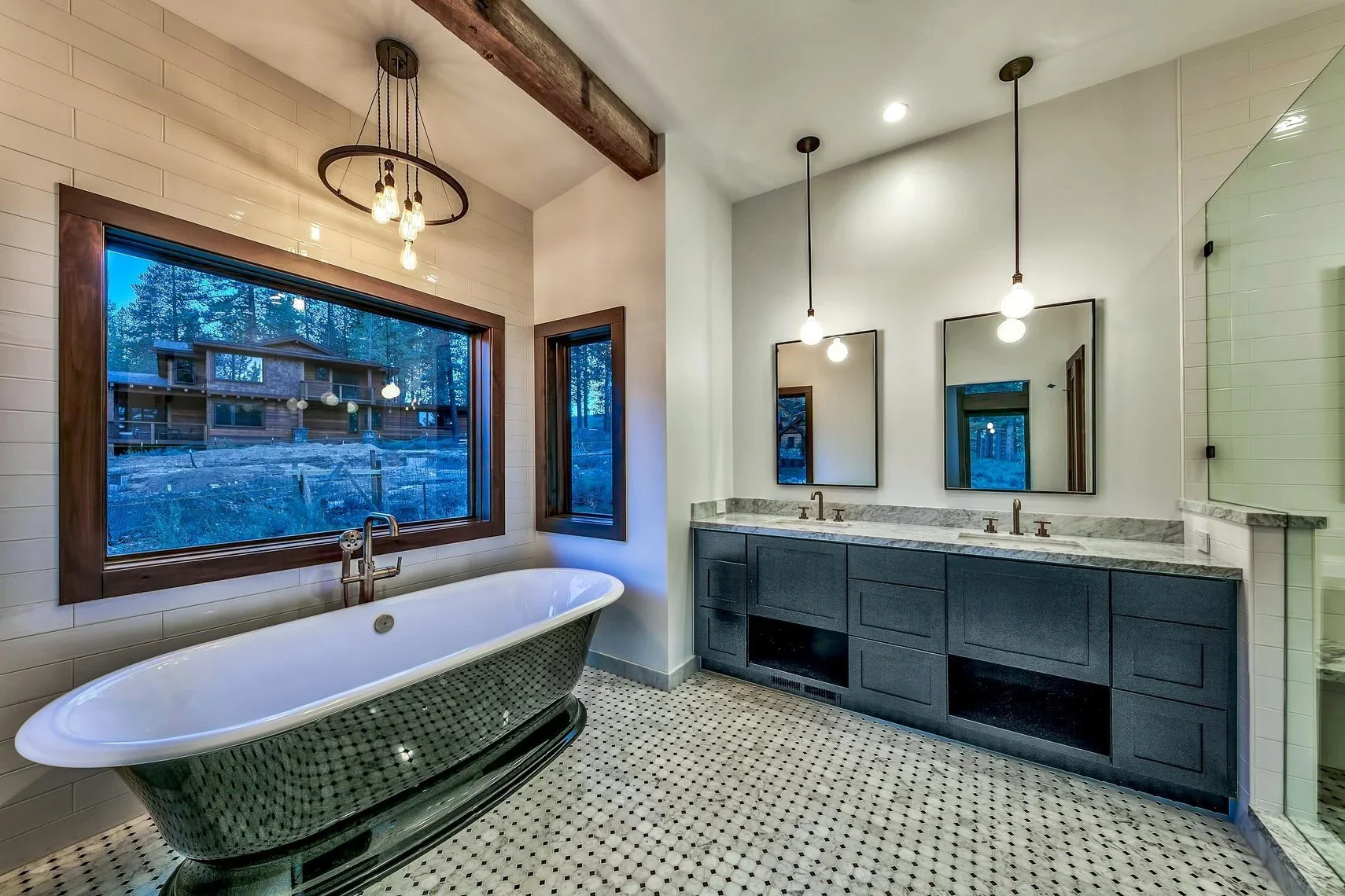 Modern bathroom with a freestanding bathtub near large windows, a double vanity with marble countertop, mirrors, and pendant lighting.