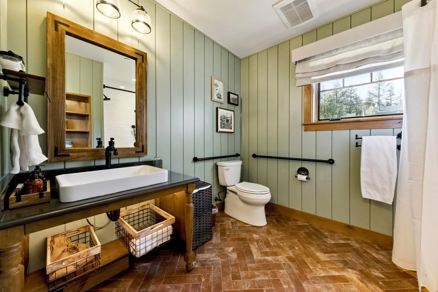 Private cabin bathroom with sage green vertical paneling, herringbone brick flooring, an open wood vanity, rectangular vessel sink, black fixtures, and a shower.