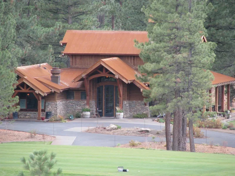 A large house with a combination of stone and wooden exterior, surrounded by tall pine trees and a well-maintained lawn.