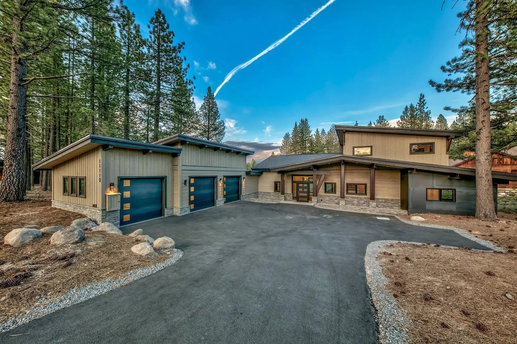 Modern house with a spacious asphalt driveway surrounded by pine trees.