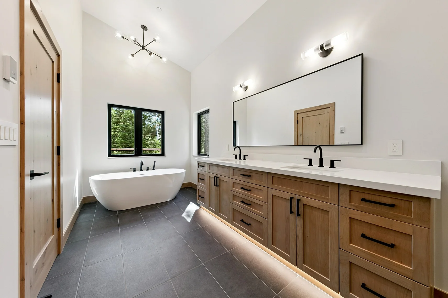 Modern bathroom with a freestanding bathtub, black fixtures, wood cabinetry, white countertops, and a double vanity with two sinks.
