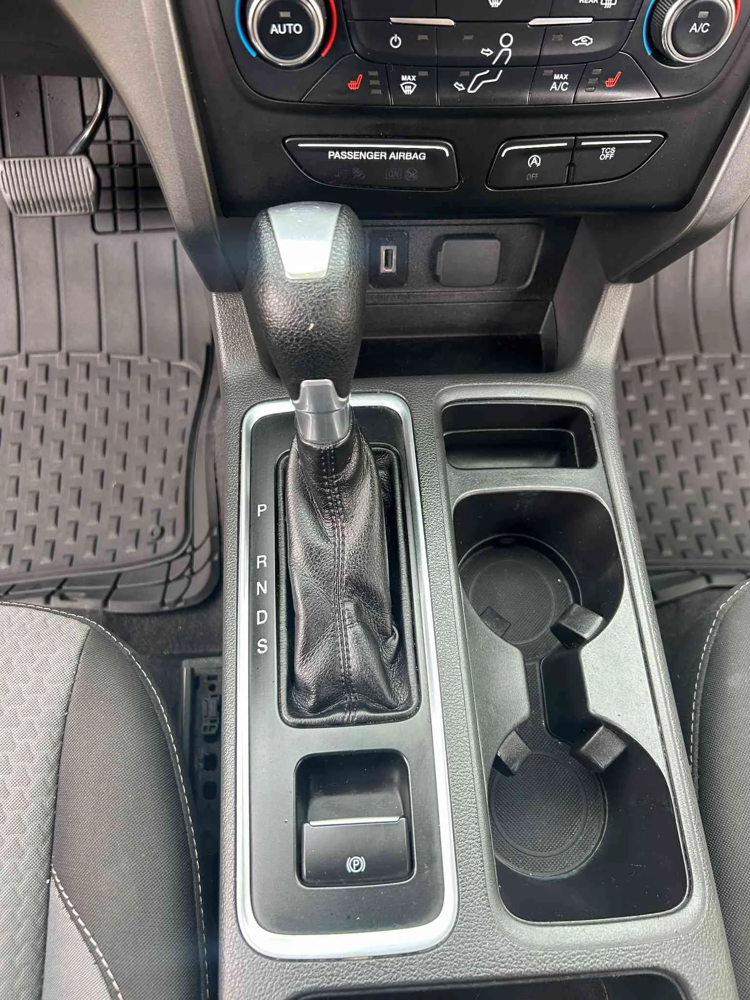 Center console of a car with gear shift, cup holders, and dashboard controls.