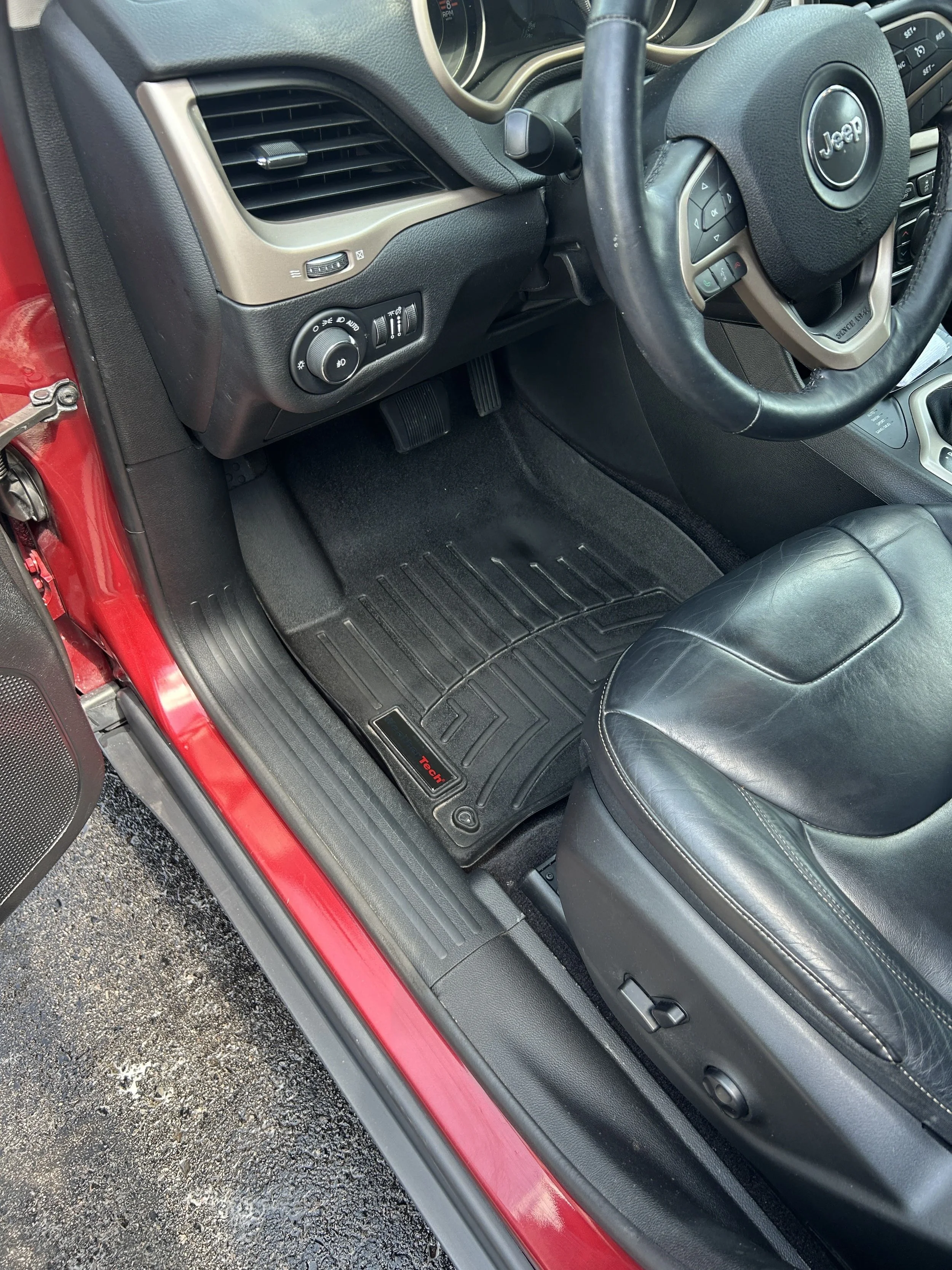 The interior of a Jeep vehicle showing the driver's seat, steering wheel, dashboard, floor mats, and pedals.